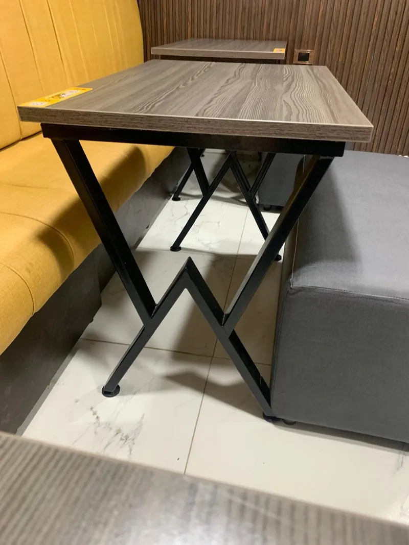 Mesa con tapa de madera y base metálica en X junto a un sofá tipo banca