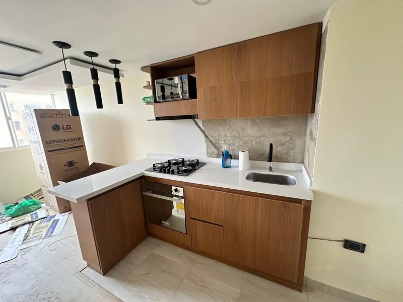 Cocina integral en L en chapa de madera tono nogal con mesón blanco, estufa y horno empotrados, en montaje