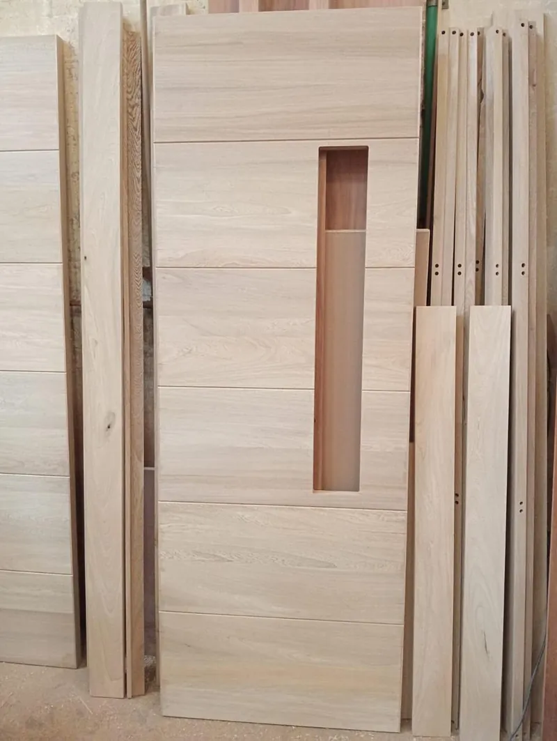 Hojas de puerta en chapa de madera apiladas en la planta de IPM, con el calado de la manija ya fresado
